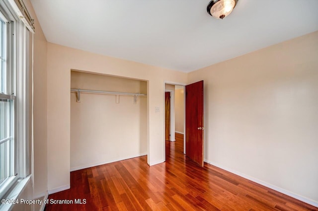 unfurnished bedroom with hardwood / wood-style floors, multiple windows, and a closet