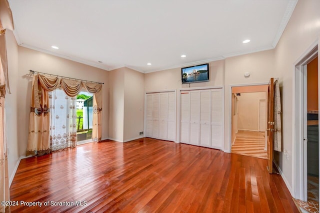 unfurnished bedroom with access to outside, crown molding, two closets, and hardwood / wood-style flooring