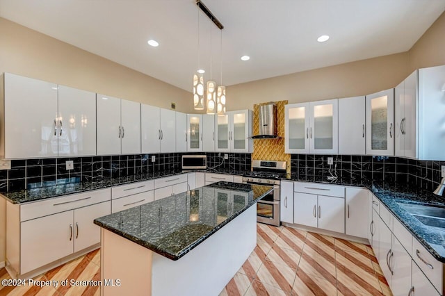 kitchen featuring wall chimney range hood, hanging light fixtures, a kitchen island, stainless steel range oven, and white cabinetry