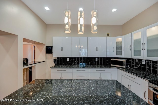 kitchen featuring backsplash, stainless steel appliances, decorative light fixtures, dark stone countertops, and white cabinets