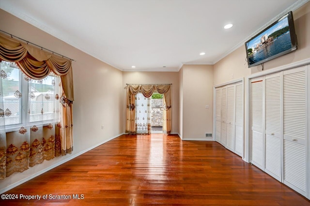 interior space featuring wood-type flooring, two closets, and crown molding