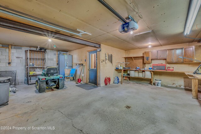 garage with a workshop area, concrete block wall, freestanding refrigerator, and a garage door opener