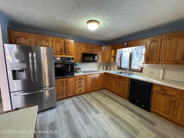 kitchen featuring light wood-style flooring, a sink, light countertops, brown cabinets, and black appliances