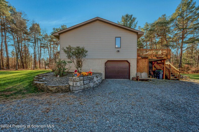 view of side of home with a lawn, an attached garage, gravel driveway, stairs, and a wooden deck