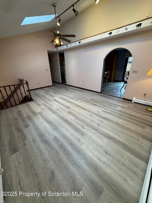 unfurnished living room with a skylight, arched walkways, wood finished floors, a baseboard heating unit, and high vaulted ceiling