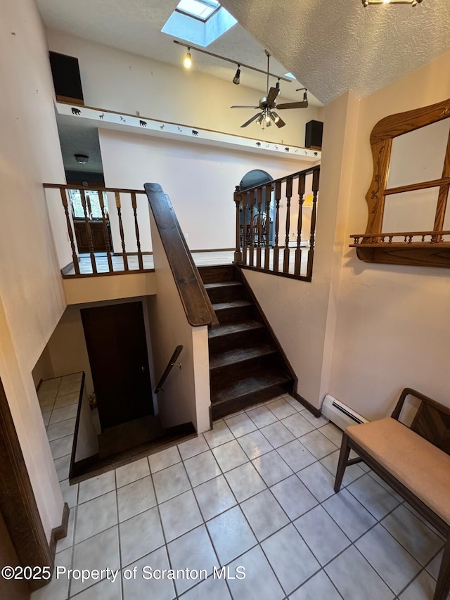 stairs with a skylight, ceiling fan, tile patterned flooring, a textured ceiling, and a baseboard heating unit