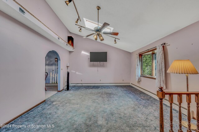 carpeted empty room featuring arched walkways, vaulted ceiling with skylight, a ceiling fan, baseboards, and rail lighting