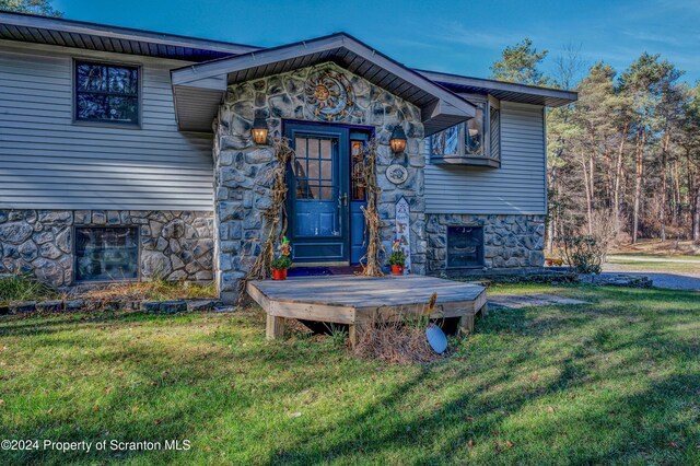 entrance to property featuring stone siding and a lawn