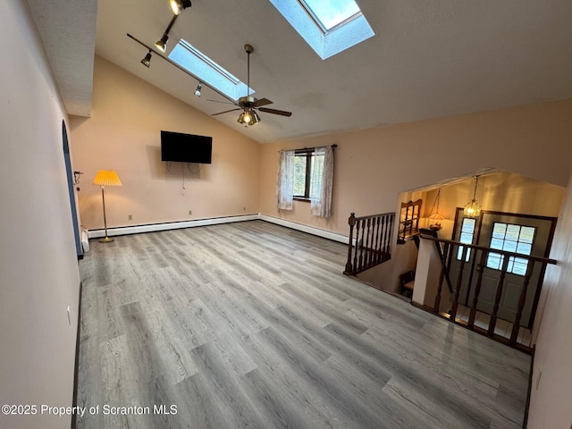 unfurnished living room featuring a skylight, baseboard heating, track lighting, wood finished floors, and high vaulted ceiling