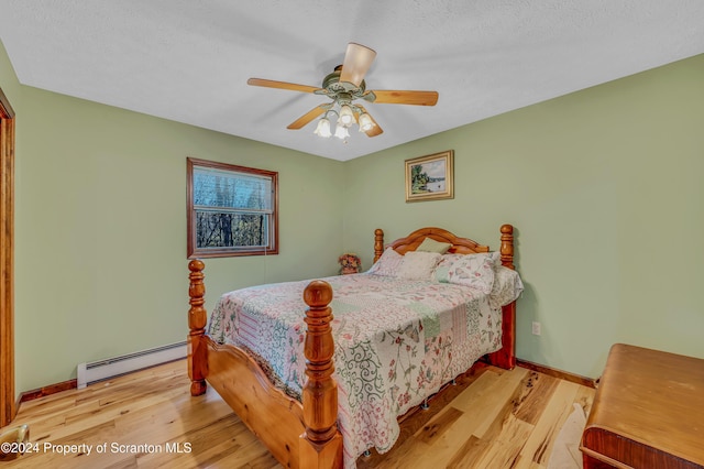 bedroom featuring a baseboard heating unit, a ceiling fan, a textured ceiling, wood finished floors, and baseboards