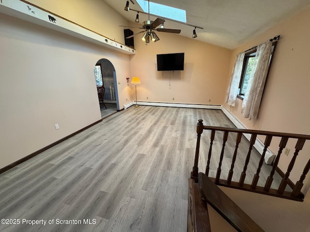 unfurnished living room with arched walkways, baseboards, lofted ceiling with skylight, a baseboard radiator, and wood finished floors