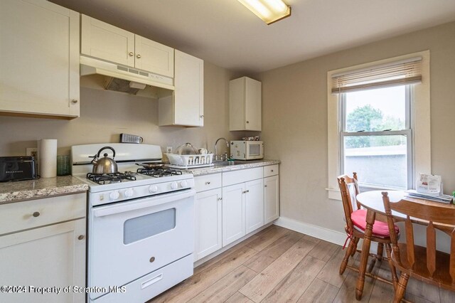 kitchen with light stone countertops, white appliances, sink, light hardwood / wood-style floors, and white cabinetry