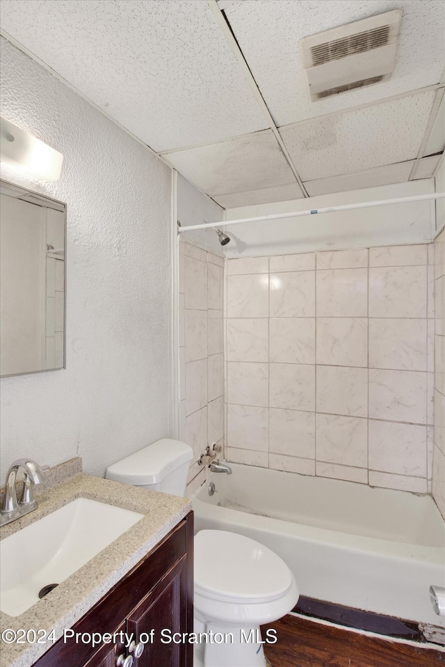 full bathroom featuring a drop ceiling, tiled shower / bath combo, hardwood / wood-style floors, toilet, and vanity