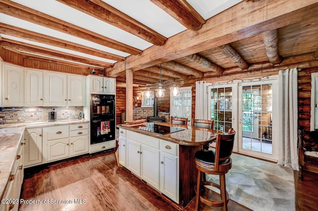 kitchen with black appliances, log walls, beamed ceiling, a kitchen island, and white cabinetry