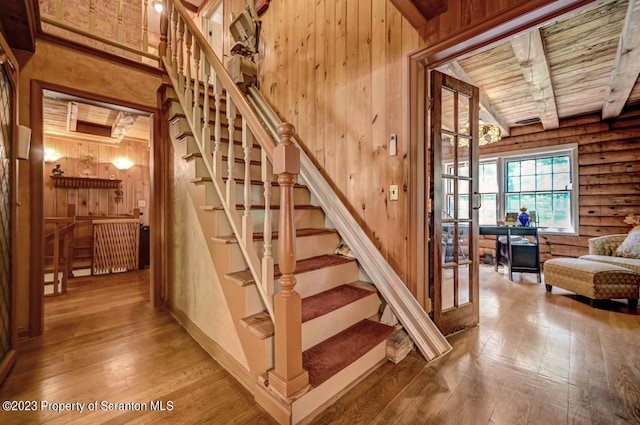 staircase with beamed ceiling, wooden ceiling, rustic walls, and hardwood / wood-style flooring