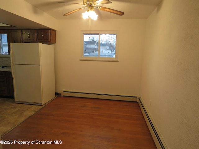 empty room featuring hardwood / wood-style flooring, ceiling fan, and baseboard heating