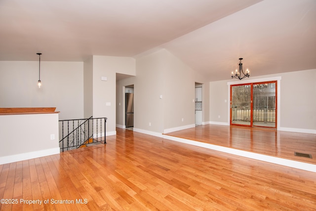 spare room with lofted ceiling, an inviting chandelier, and light hardwood / wood-style flooring