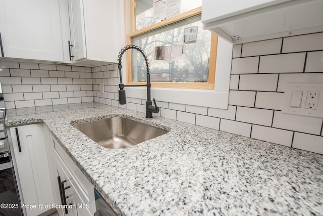 kitchen featuring white cabinetry, sink, light stone counters, and decorative backsplash