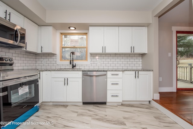 kitchen featuring appliances with stainless steel finishes, tasteful backsplash, light stone countertops, sink, and white cabinetry