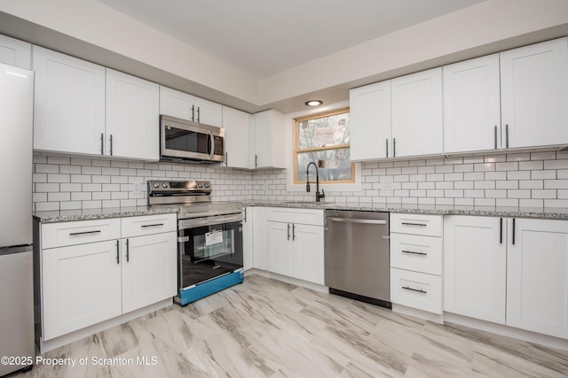 kitchen with sink, stainless steel appliances, white cabinets, light stone countertops, and tasteful backsplash