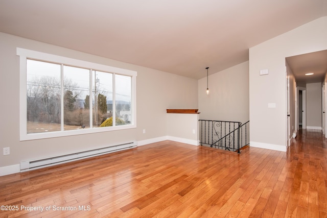 unfurnished room featuring light wood-type flooring, vaulted ceiling, and a baseboard heating unit