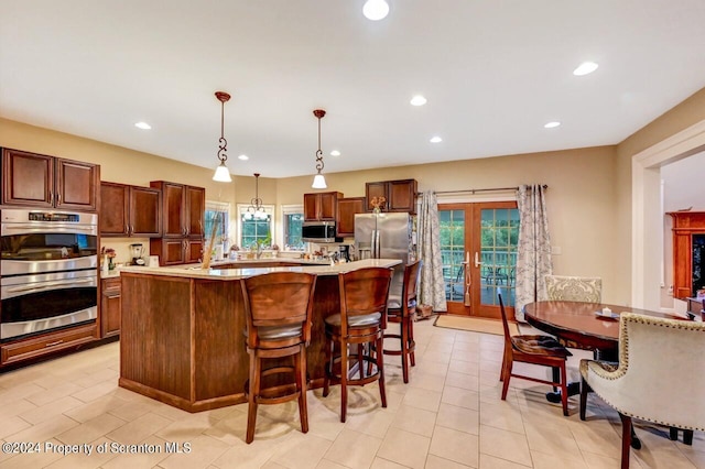 kitchen featuring french doors, a center island with sink, hanging light fixtures, light tile patterned floors, and appliances with stainless steel finishes