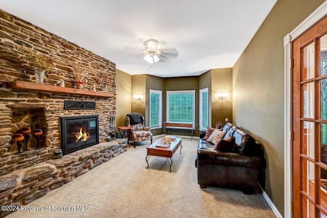 living room featuring carpet, a stone fireplace, and ceiling fan