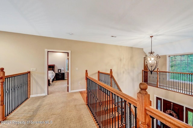 corridor featuring light colored carpet, lofted ceiling, and an inviting chandelier