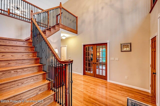 stairs with french doors, a towering ceiling, and wood-type flooring