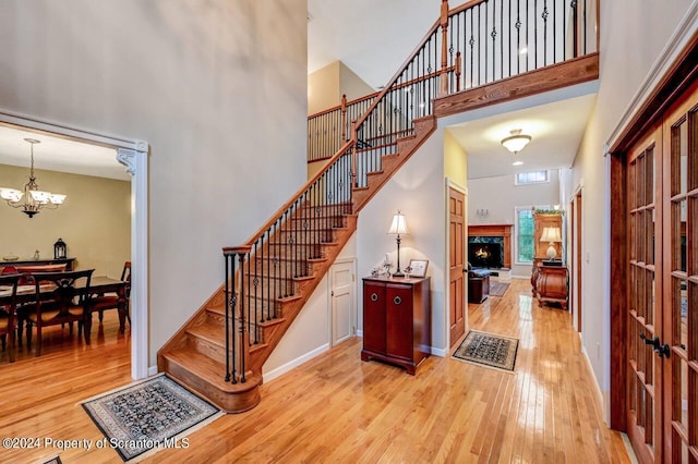 stairway with an inviting chandelier, a high end fireplace, a high ceiling, and hardwood / wood-style flooring