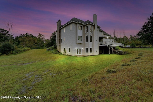 back house at dusk with a wooden deck and a lawn