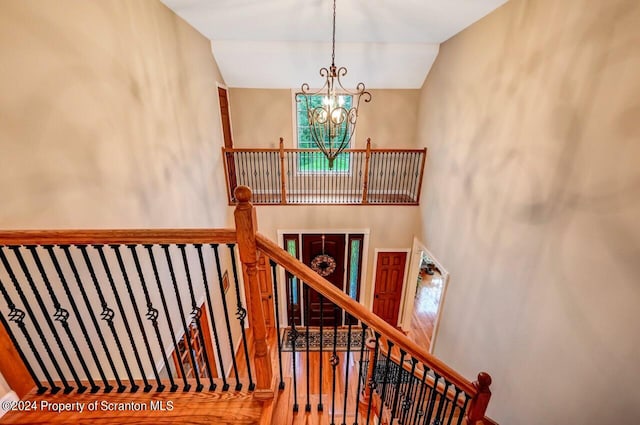 staircase with wood-type flooring, a towering ceiling, and a chandelier