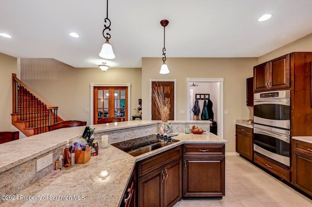 kitchen featuring light stone counters, double oven, decorative light fixtures, black electric stovetop, and light tile patterned flooring