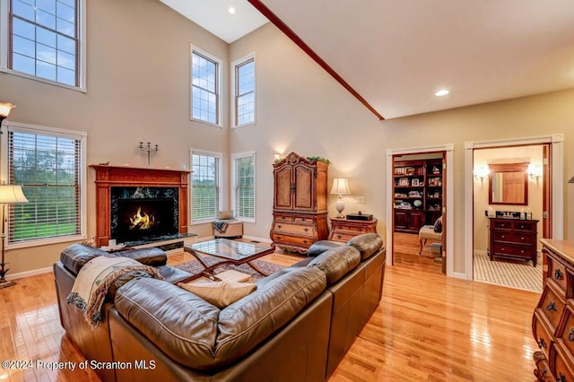 living room with a premium fireplace, a towering ceiling, and light hardwood / wood-style floors