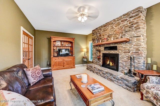 living room featuring a stone fireplace, ceiling fan, and light colored carpet