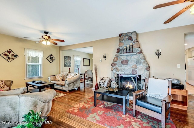 living room with a fireplace, ceiling fan, and wood-type flooring