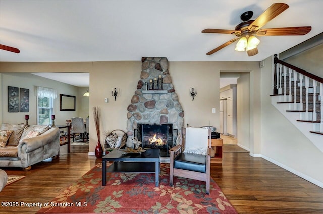 living room with a fireplace, ceiling fan, and dark wood-type flooring