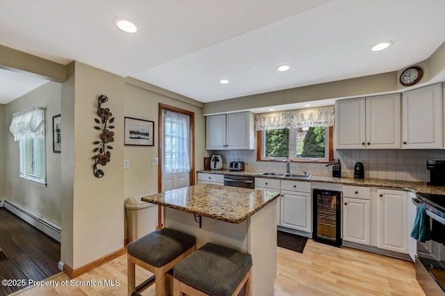 kitchen featuring light stone countertops, a baseboard heating unit, light wood-type flooring, wine cooler, and sink