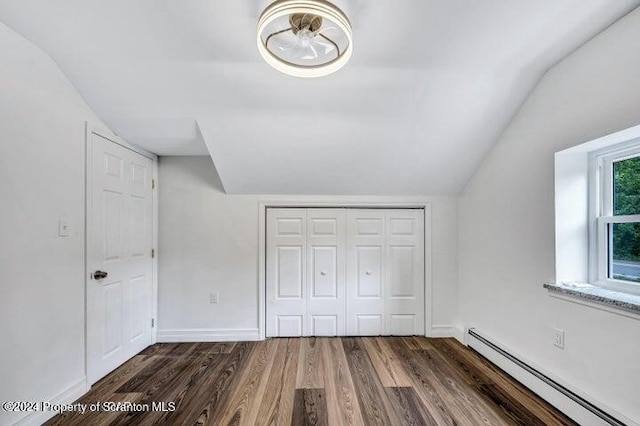 unfurnished bedroom featuring a closet, dark hardwood / wood-style flooring, baseboard heating, and vaulted ceiling