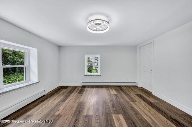 empty room with dark wood-type flooring, a wealth of natural light, and a baseboard heating unit