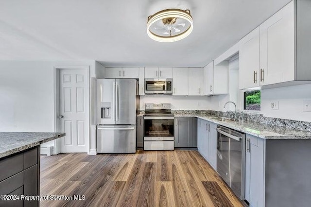 kitchen with light stone countertops, appliances with stainless steel finishes, white cabinetry, and hardwood / wood-style floors