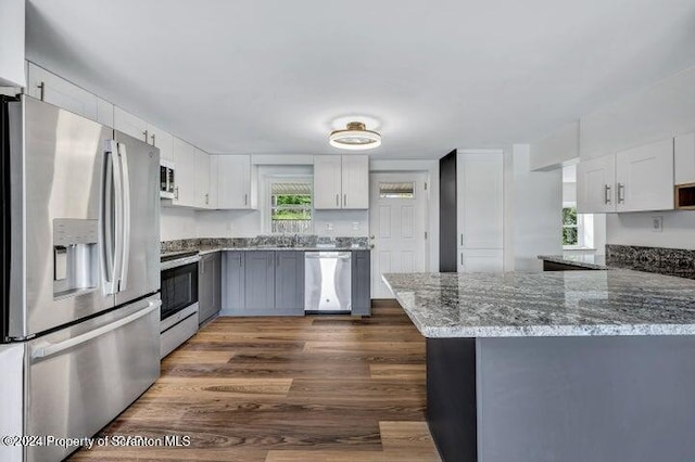 kitchen featuring dark stone counters, white cabinetry, stainless steel appliances, and dark hardwood / wood-style floors