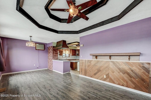 unfurnished living room with wood finished floors, a wall unit AC, and a ceiling fan