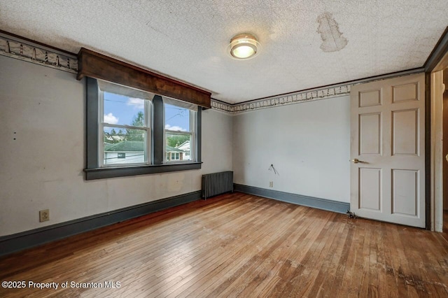 unfurnished room with a textured ceiling, baseboards, ornamental molding, radiator, and wood-type flooring