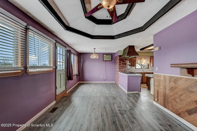 interior space featuring a raised ceiling, a ceiling fan, wood finished floors, baseboards, and visible vents