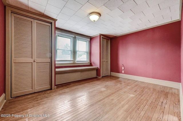 unfurnished bedroom featuring baseboards, two closets, and hardwood / wood-style floors