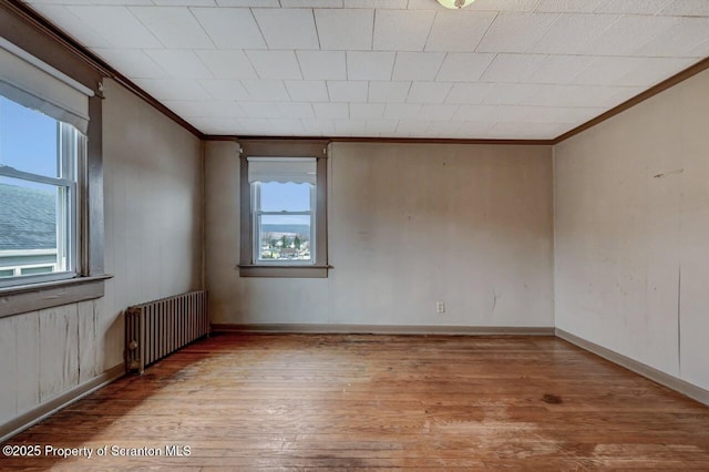unfurnished room featuring radiator heating unit, ornamental molding, baseboards, and wood finished floors