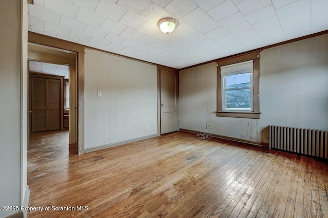 unfurnished room featuring baseboards, light wood-type flooring, radiator heating unit, and ornamental molding