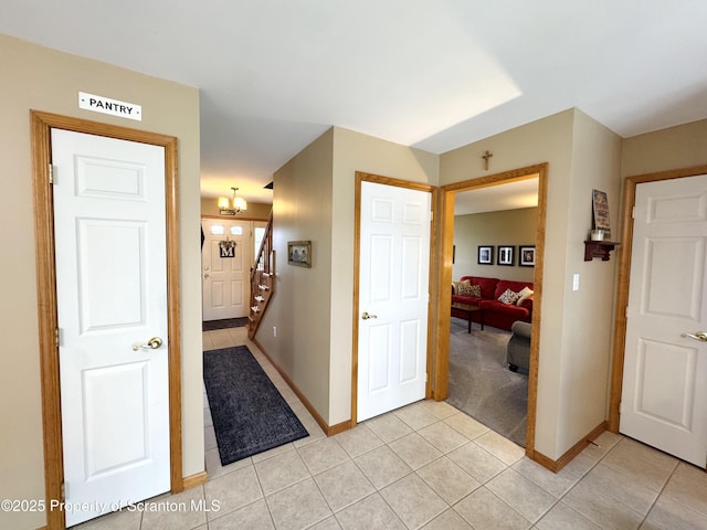 hall featuring light tile patterned floors, baseboards, light colored carpet, and stairway
