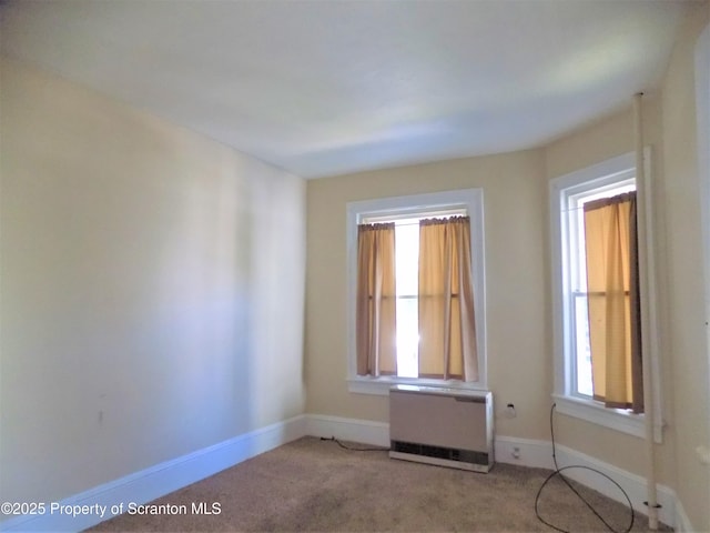 empty room with carpet flooring, heating unit, and a wealth of natural light